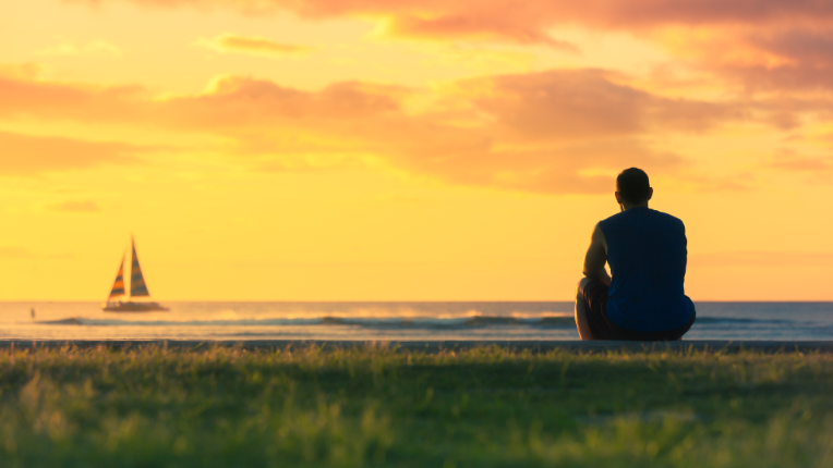 Man looking out to a ship during a sunset