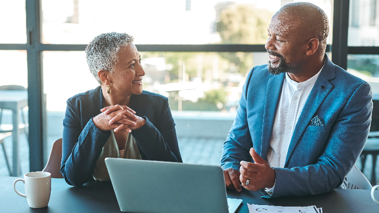 Smartly dressed elderly man and woman smiling and having a discussion, seated in front of a laptop