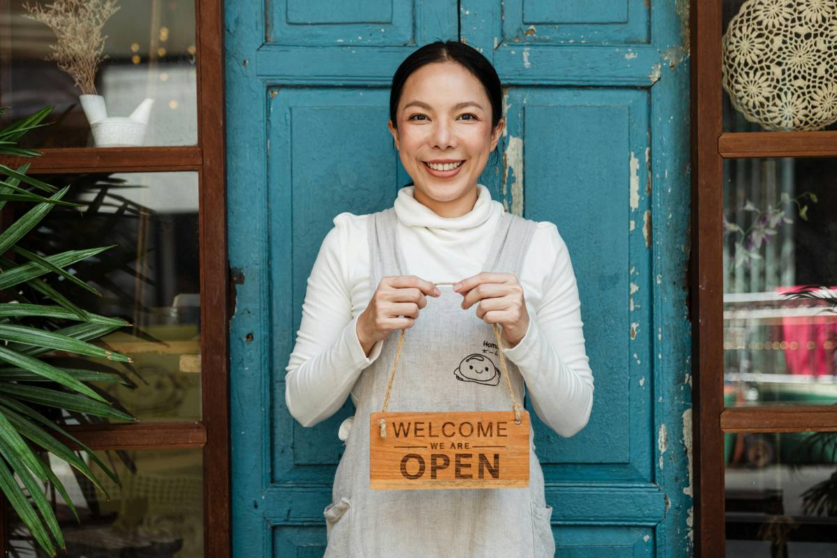 Woman holding a Welcome we are open sign in front of a blue door