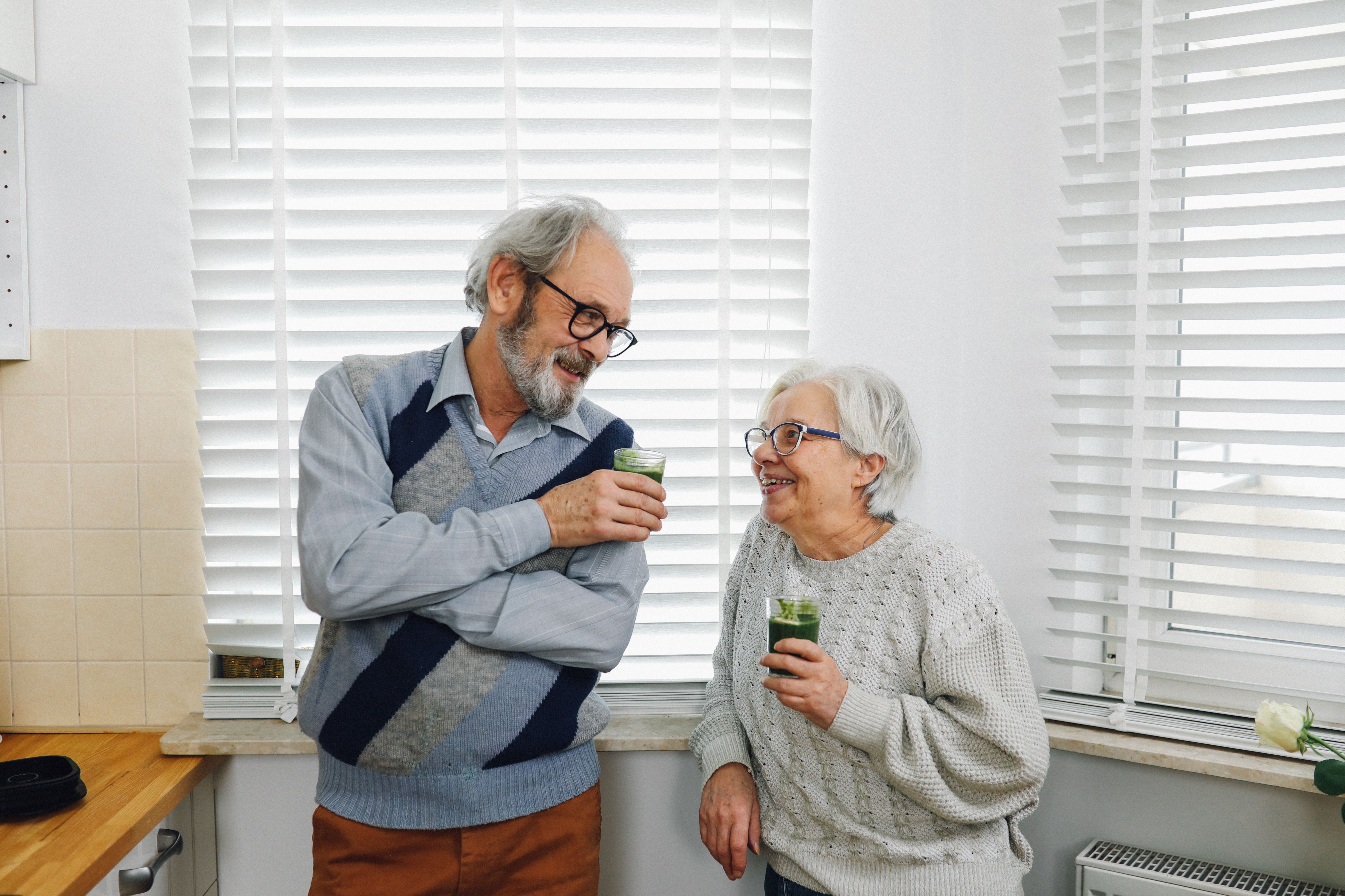 An elderly couple in their 70s holding an heathy drionk and looking at each other
