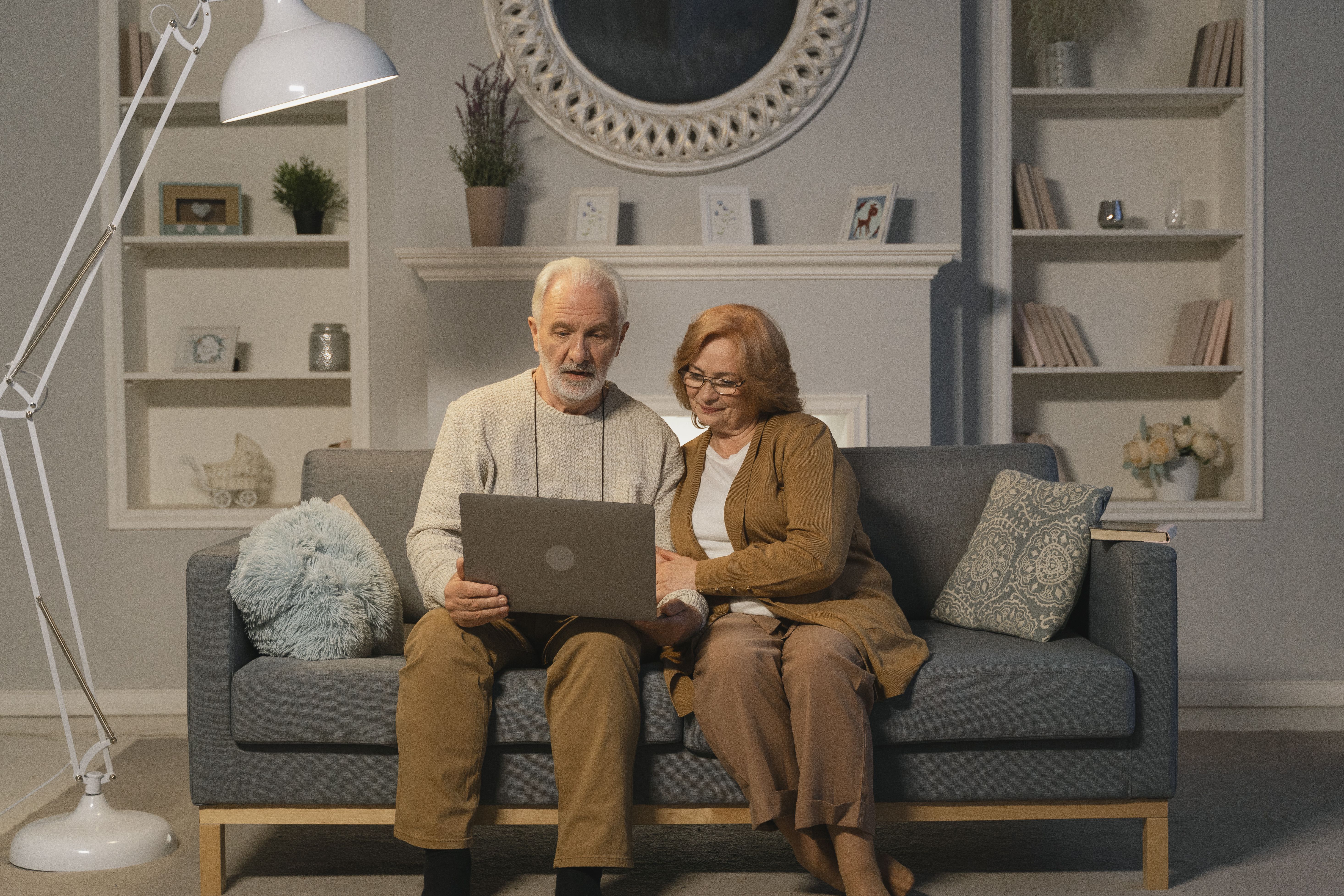 A retired couple sitting on a couch and looing at a laptop screen